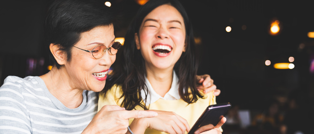 A young woman and her older mom laughing at something on a smartphone.