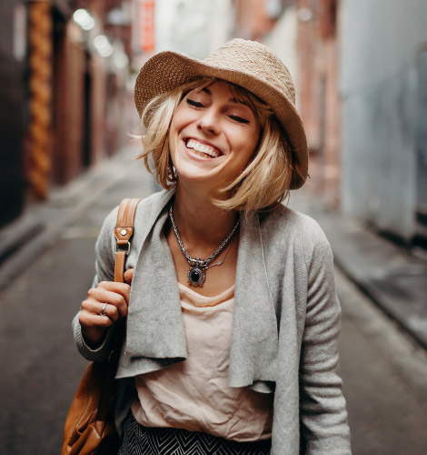 Smiling young woman in a hat standing in a city alley.