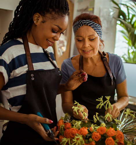 A young woman and an older woman in aprons, they are arranging some flowers.