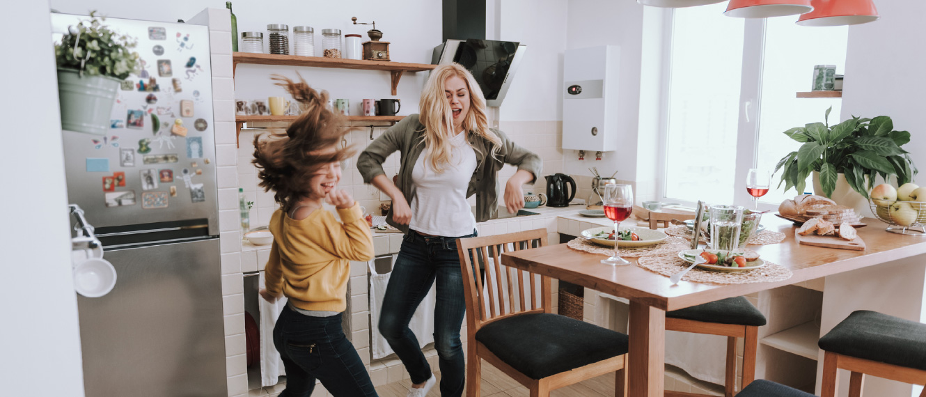 A young woman and a teenage girl dancing in a kitchen.