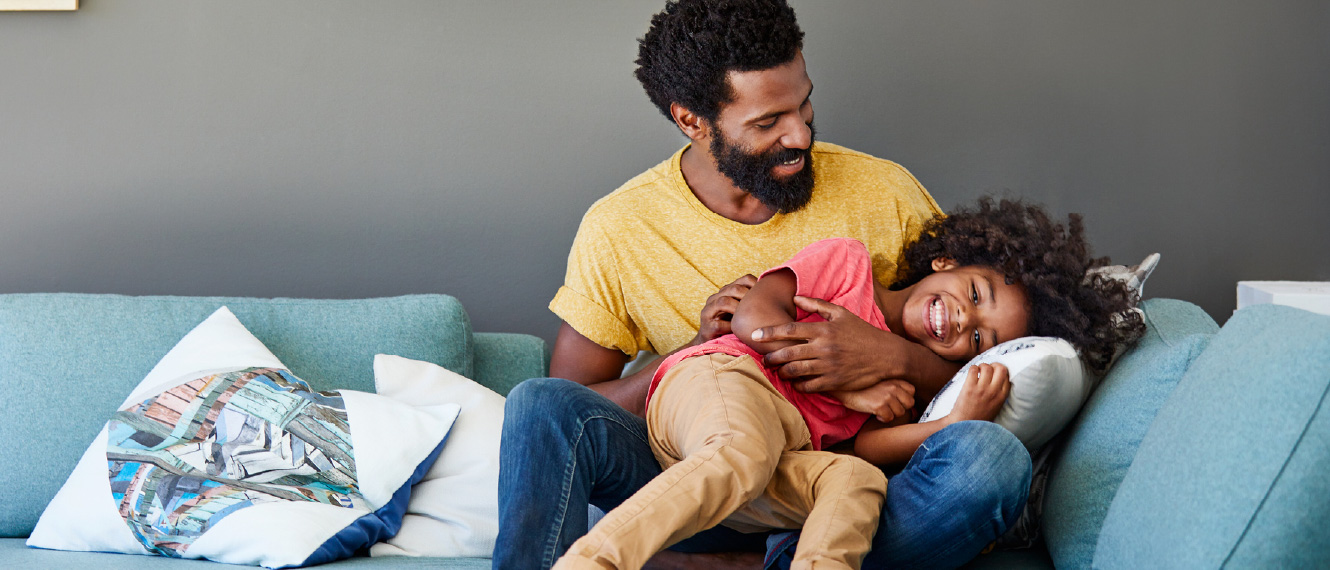 Dad and kid rough housing on a blue couch.