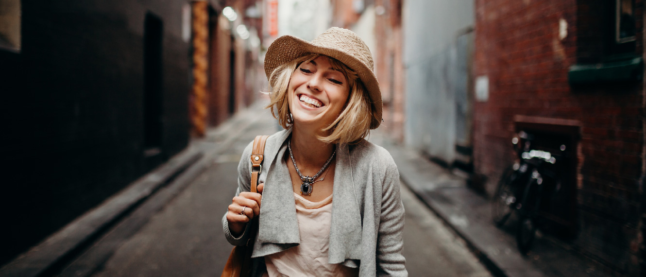 A young woman standing in a city alley, she's smiling.