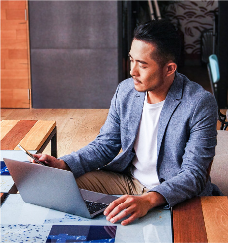 Man sitting at a desk with a laptop looking at his phone.