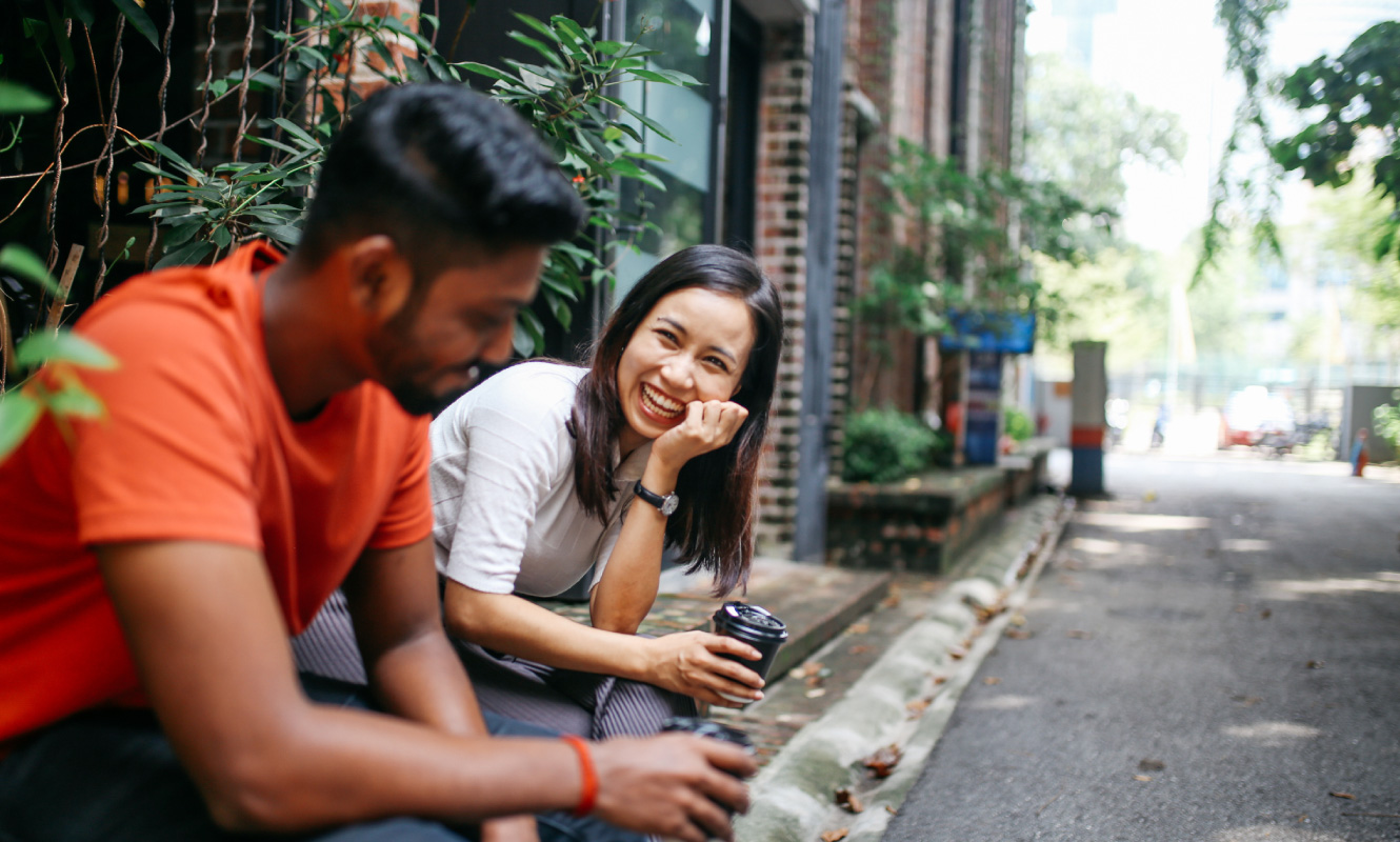 A man and woman sitting outside a building with coffee cups in their hands.