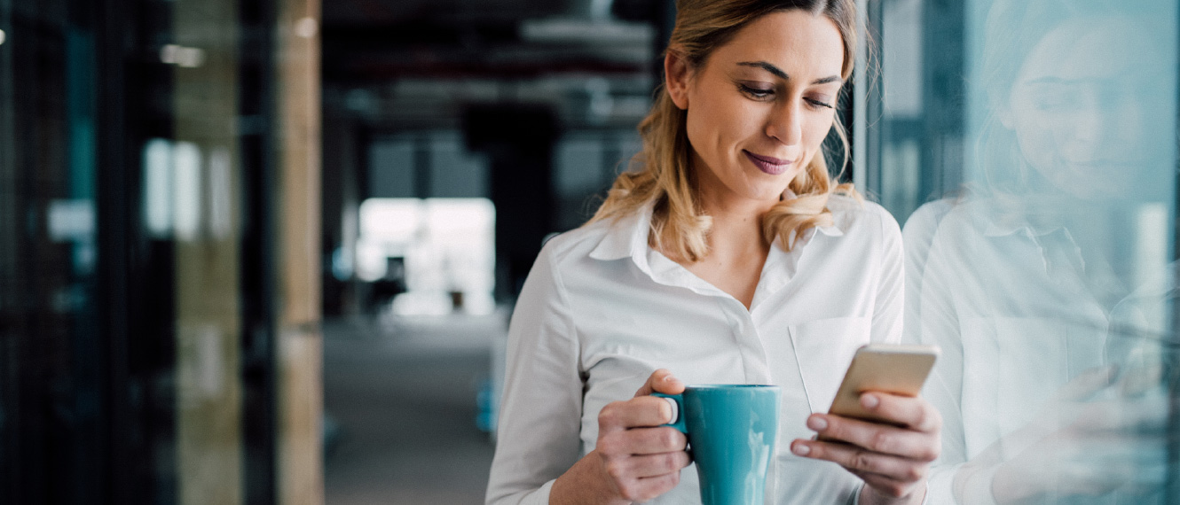 A woman in business attire holding a coffee mug and smartphone.