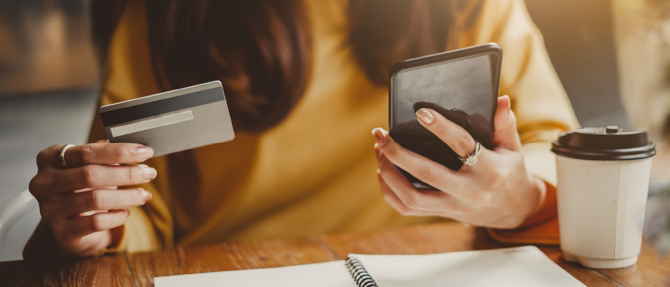 Close up of a woman's hands, one is holding a credit card and the other is holding a smartphone.