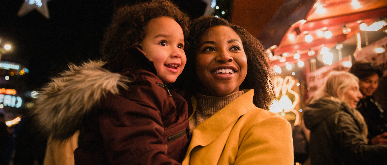 A mom holding her kid outside in warm coats.