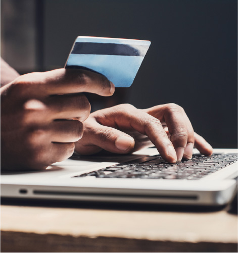 Close up of hands holding a credit card over a laptop keyboard.